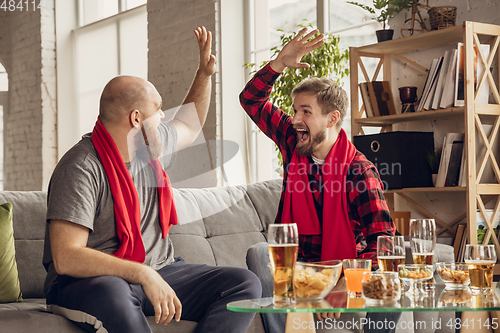 Image of Excited, happy friends watch sport match together on the couch at home
