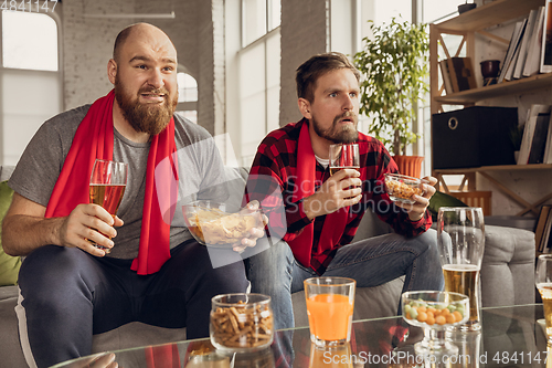 Image of Excited, happy friends watch sport match together on the couch at home