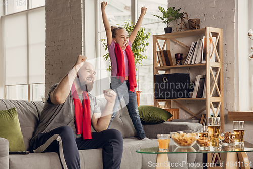 Image of Excited, happy daughter and father watch football, soccer match together on the couch at home