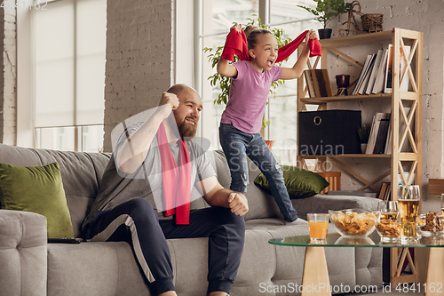 Image of Excited, happy daughter and father watch football, soccer match together on the couch at home