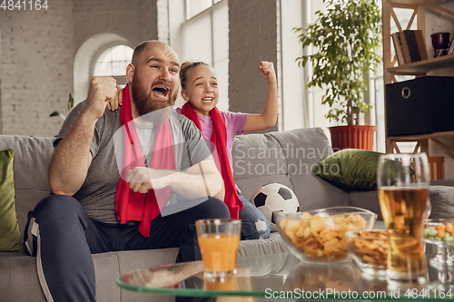 Image of Excited, happy daughter and father watch football, soccer match together on the couch at home
