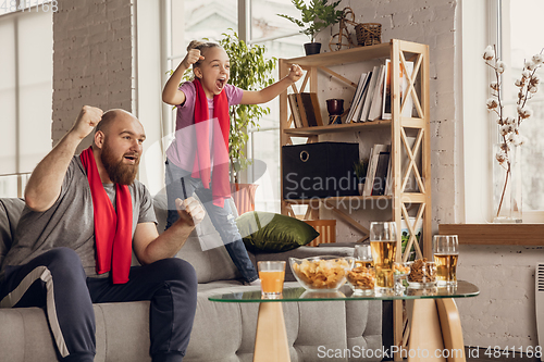 Image of Excited, happy daughter and father watch football, soccer match together on the couch at home
