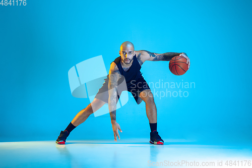 Image of Young basketball player training isolated on blue studio background in neon light