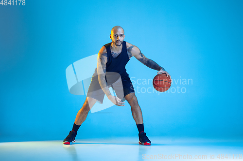 Image of Young basketball player training isolated on blue studio background in neon light