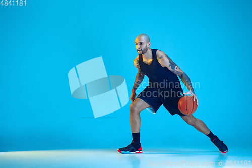 Image of Young basketball player training isolated on blue studio background in neon light