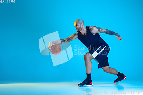 Image of Young basketball player training isolated on blue studio background in neon light