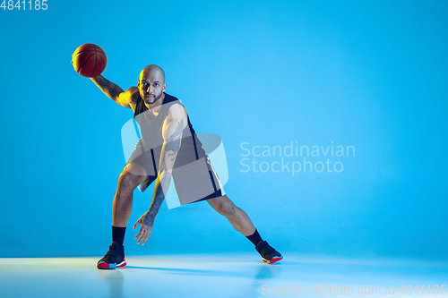 Image of Young basketball player training isolated on blue studio background in neon light