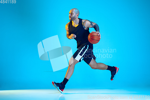 Image of Young basketball player training isolated on blue studio background in neon light