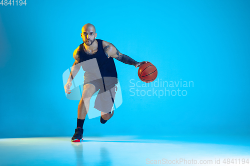 Image of Young basketball player training isolated on blue studio background in neon light