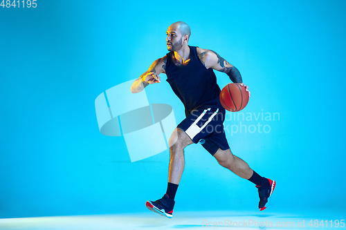 Image of Young basketball player training isolated on blue studio background in neon light