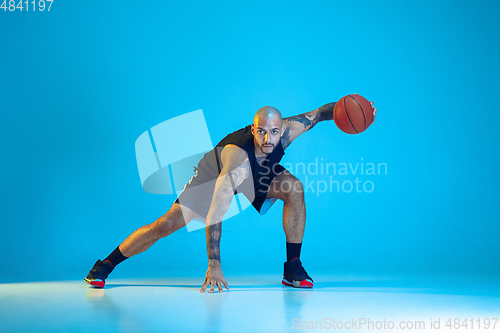 Image of Young basketball player training isolated on blue studio background in neon light