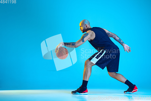 Image of Young basketball player training isolated on blue studio background in neon light