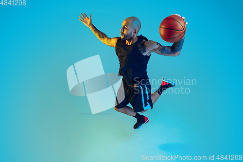 Image of Young basketball player training isolated on blue studio background in neon light