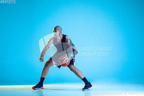 Image of Young basketball player training isolated on blue studio background in neon light