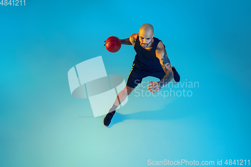 Image of Young basketball player training isolated on blue studio background in neon light