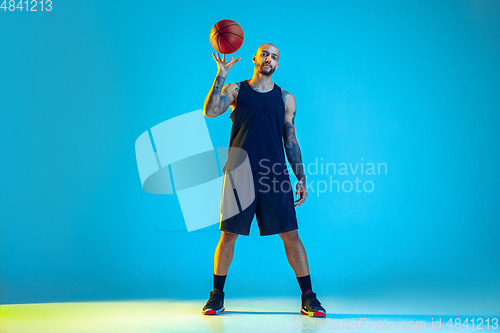 Image of Young basketball player training isolated on blue studio background in neon light