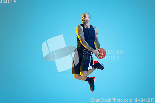 Image of Young basketball player training isolated on blue studio background in neon light