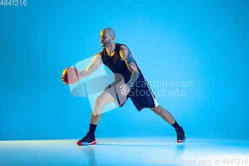 Image of Young basketball player training isolated on blue studio background in neon light