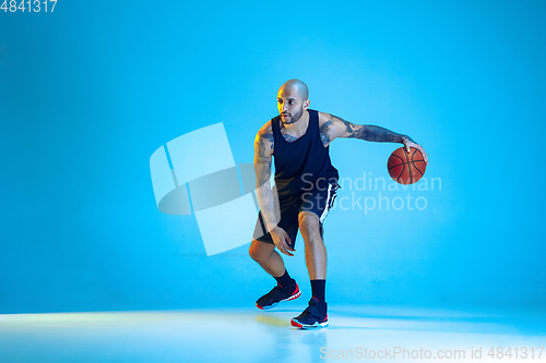 Image of Young basketball player training isolated on blue studio background in neon light