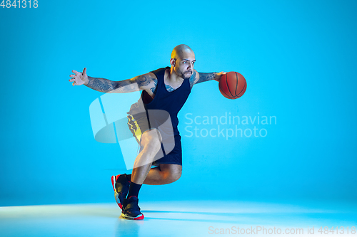 Image of Young basketball player training isolated on blue studio background in neon light