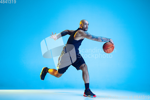 Image of Young basketball player training isolated on blue studio background in neon light