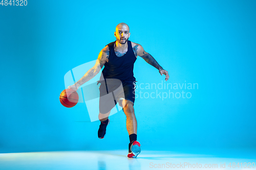 Image of Young basketball player training isolated on blue studio background in neon light