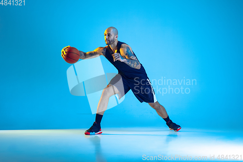 Image of Young basketball player training isolated on blue studio background in neon light