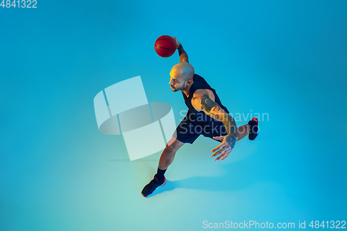 Image of Young basketball player training isolated on blue studio background in neon light