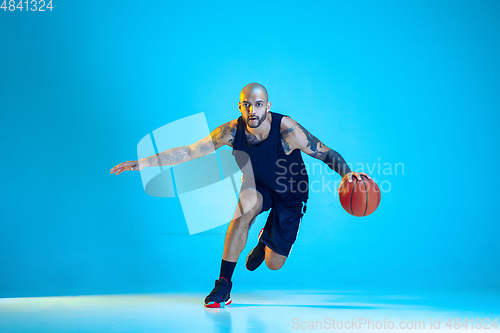 Image of Young basketball player training isolated on blue studio background in neon light