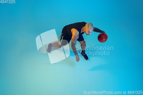 Image of Young basketball player training isolated on blue studio background in neon light