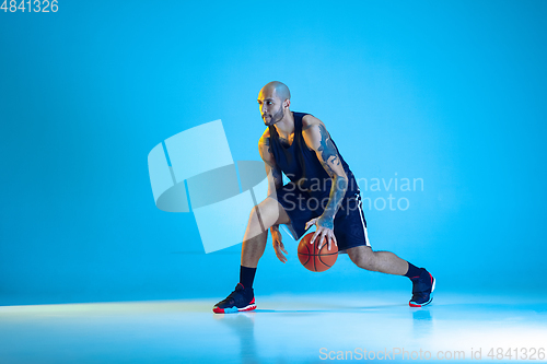 Image of Young basketball player training isolated on blue studio background in neon light