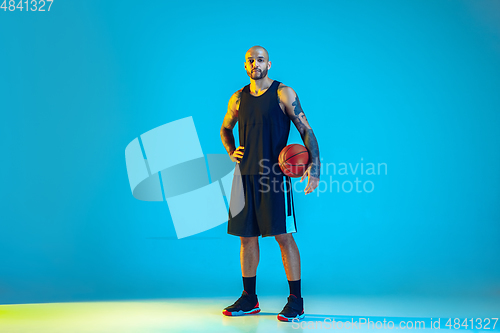 Image of Young basketball player training isolated on blue studio background in neon light