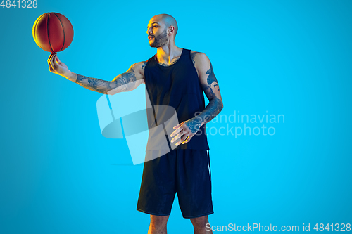 Image of Young basketball player training isolated on blue studio background in neon light