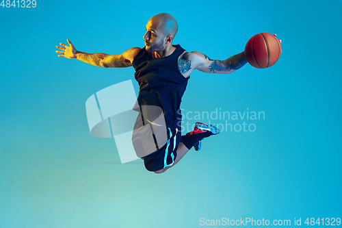 Image of Young basketball player training isolated on blue studio background in neon light