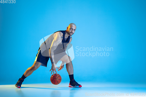 Image of Young basketball player training isolated on blue studio background in neon light