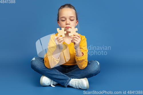 Image of Portrait of sad little girl sitting on blue studio background, autism concept