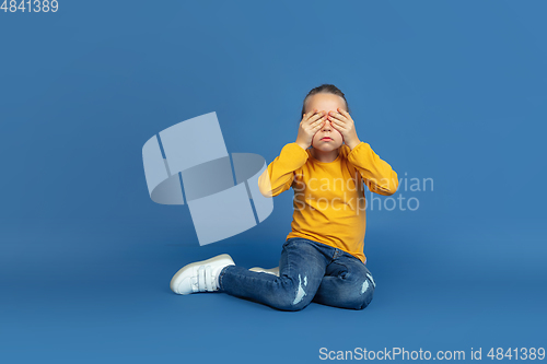 Image of Portrait of sad little girl sitting on blue studio background, autism concept