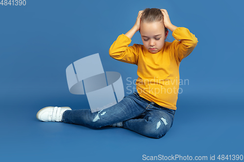 Image of Portrait of sad little girl sitting on blue studio background, autism concept