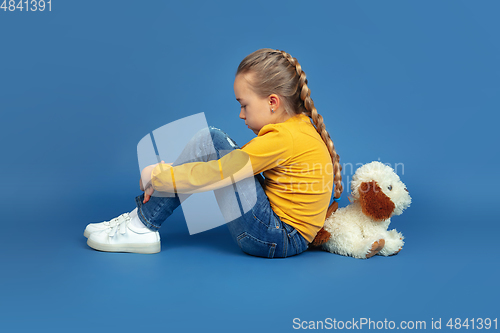 Image of Portrait of sad little girl sitting on blue studio background, autism concept