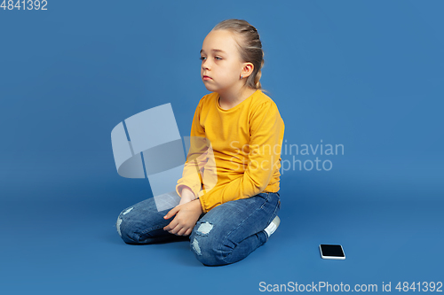 Image of Portrait of sad little girl sitting on blue studio background, autism concept