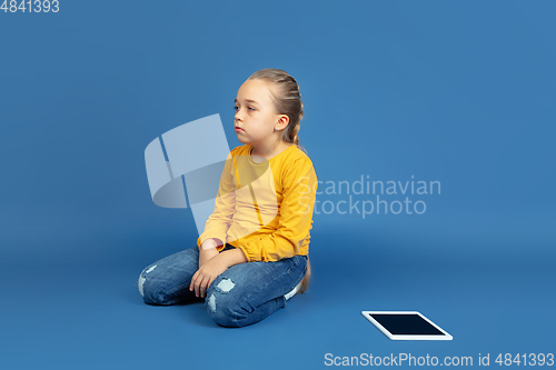 Image of Portrait of sad little girl sitting on blue studio background, autism concept