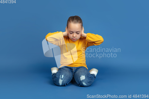 Image of Portrait of sad little girl sitting on blue studio background, autism concept