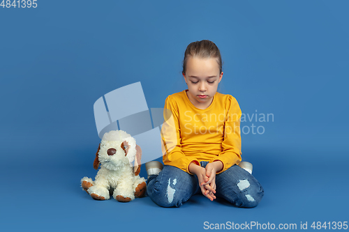 Image of Portrait of sad little girl sitting on blue studio background, autism concept