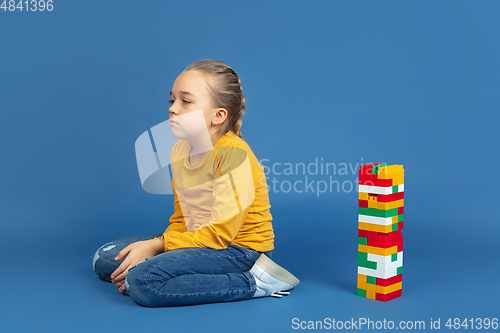 Image of Portrait of sad little girl sitting on blue studio background, autism concept