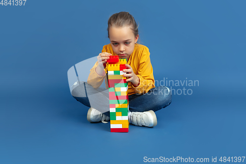 Image of Portrait of sad little girl sitting on blue studio background, autism concept