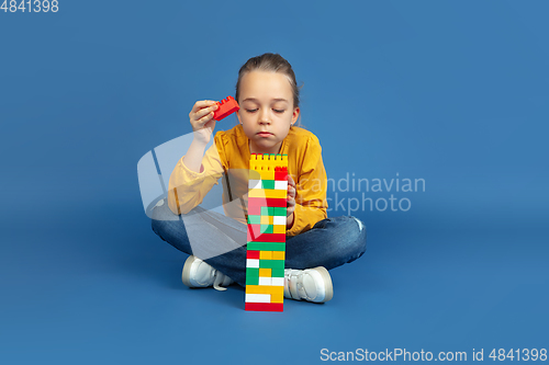 Image of Portrait of sad little girl sitting on blue studio background, autism concept