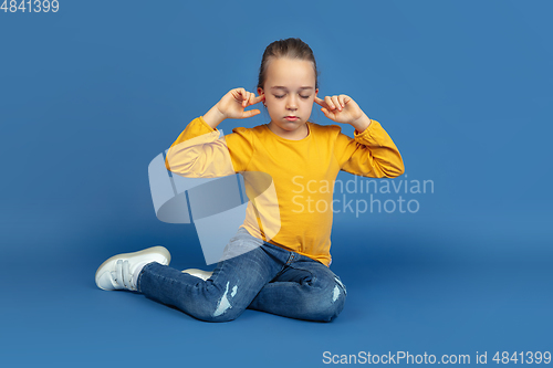 Image of Portrait of sad little girl sitting on blue studio background, autism concept