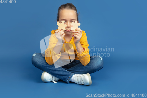 Image of Portrait of sad little girl sitting on blue studio background, autism concept