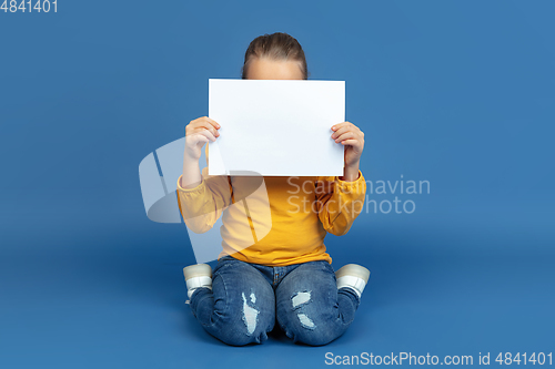 Image of Portrait of sad little girl sitting on blue studio background, autism concept