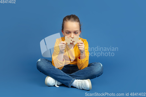 Image of Portrait of sad little girl sitting on blue studio background, autism concept